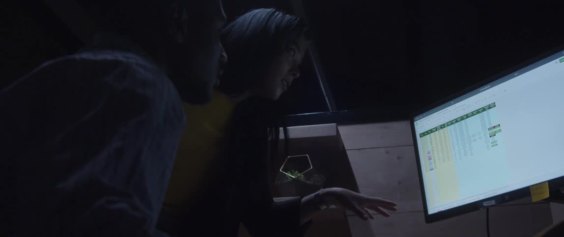 Two employees having a discussion in front of a computer monitor in a dark office