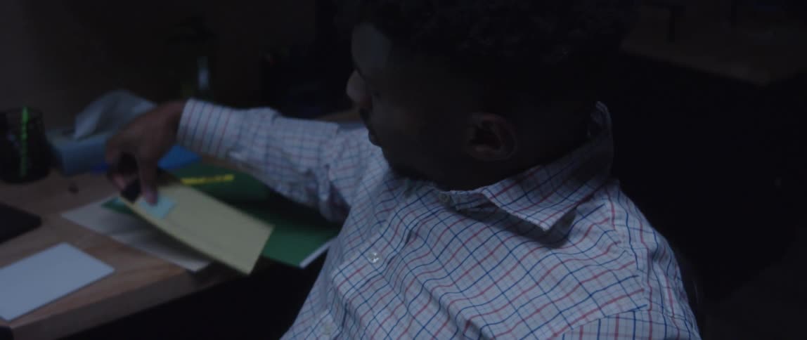 A man sitting at a desk stretches before beginning to write on a notepad