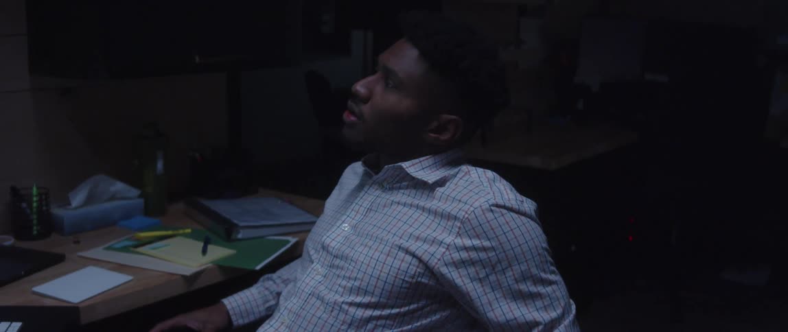 Tired man working in office wipes his eyes then leans back in his chair