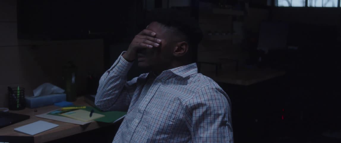 Man working in office leans back to rub his face before returning to work