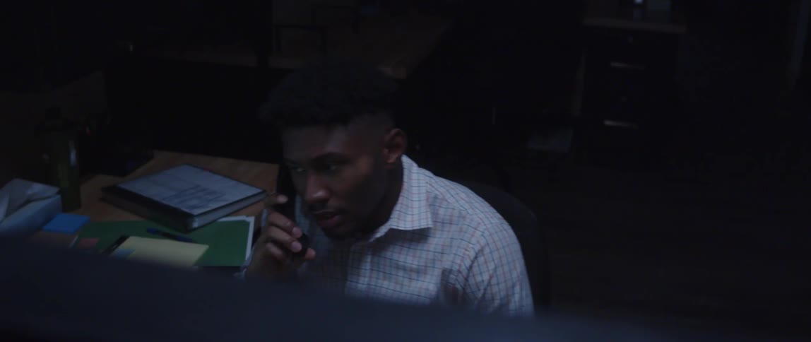 A man talks on an office phone in a dimly lit office at night