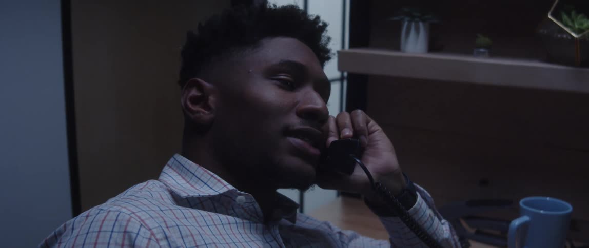 A man is sitting at a desk talking on the telephone in his office
