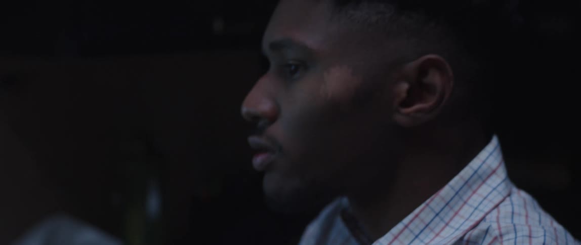 Light from a computer monitor shines on the face of a man sitting at a desk working