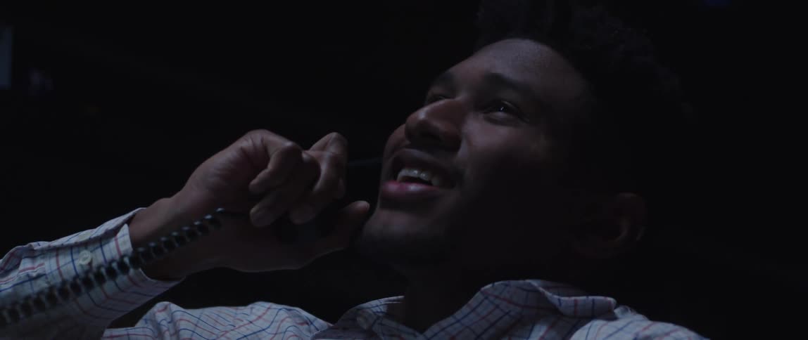 A mans face talking on the phone smiling while he sits in a chair