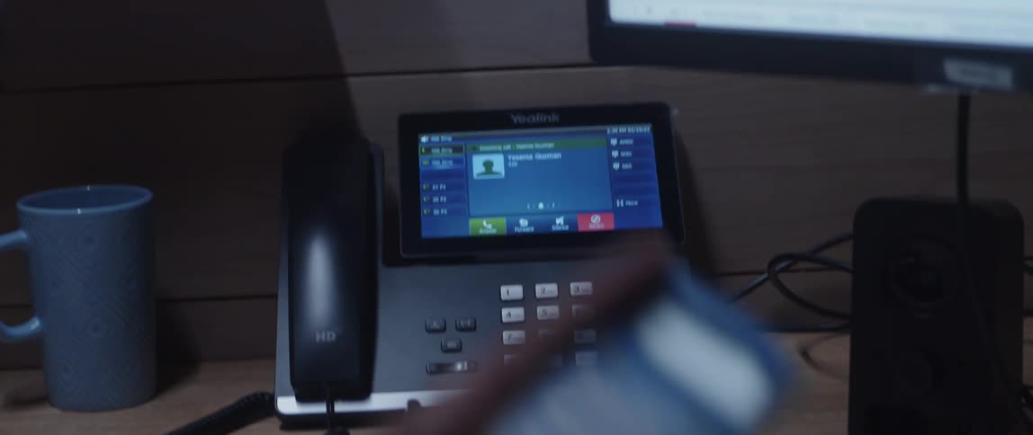 A calculator held by a man sitting at his desk and then picking up his phone that rings