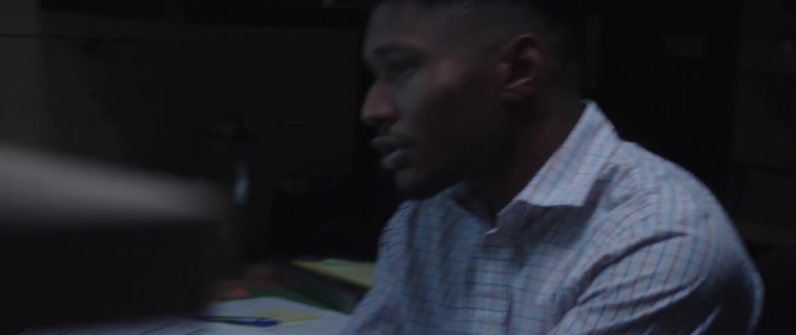Black man in office talking on speakerphone while typing on computer keyboard