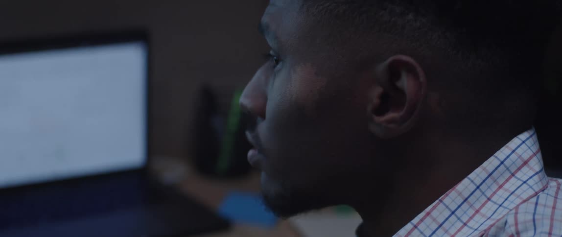 A man is sitting at a desk with computers as he looks at a monitor