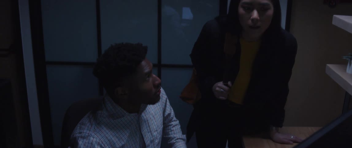 Two office workers are collaborating in a cubicle while staring at a computer monitor