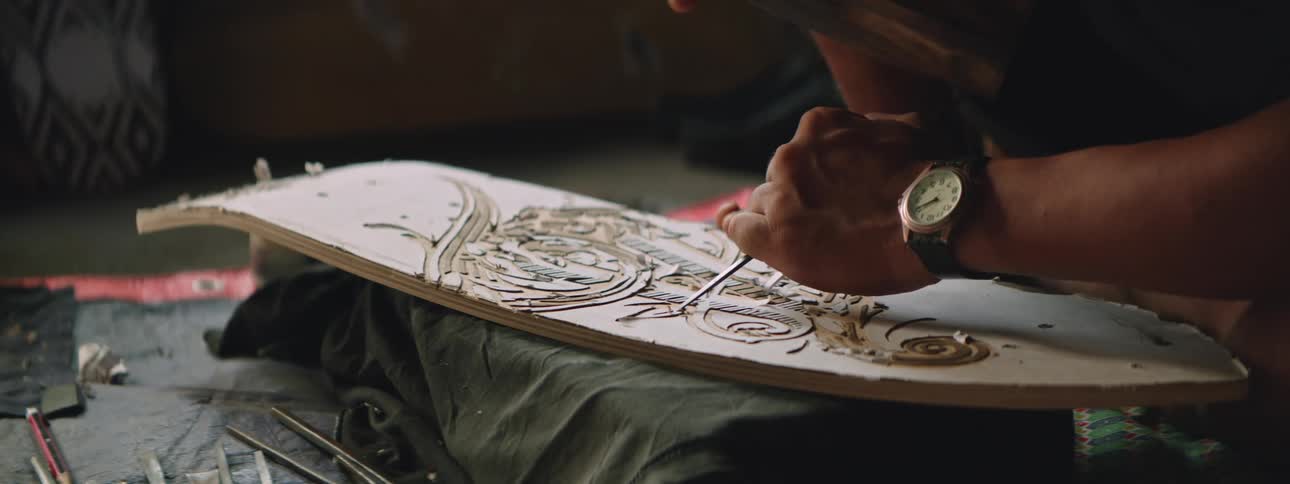 A man creates an art piece by carving a design into a slab of wood