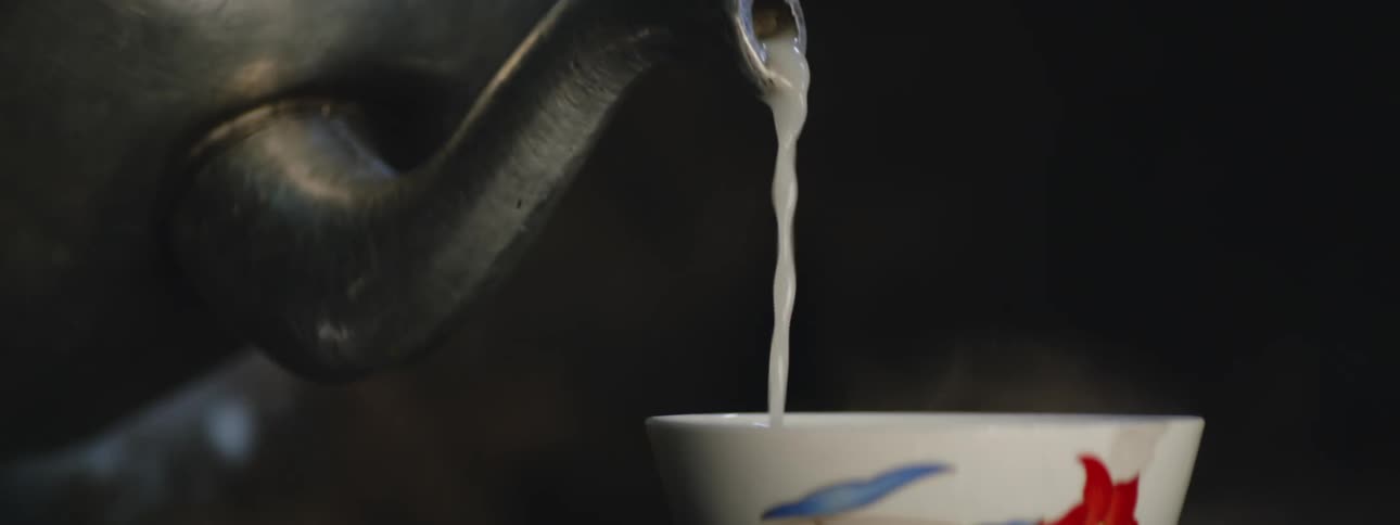 An up close of a black tea pot pouring a liquid into a tea cup