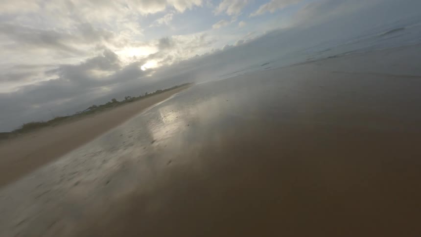 Aerial view of ocean waves breaking against beach sand at sunset