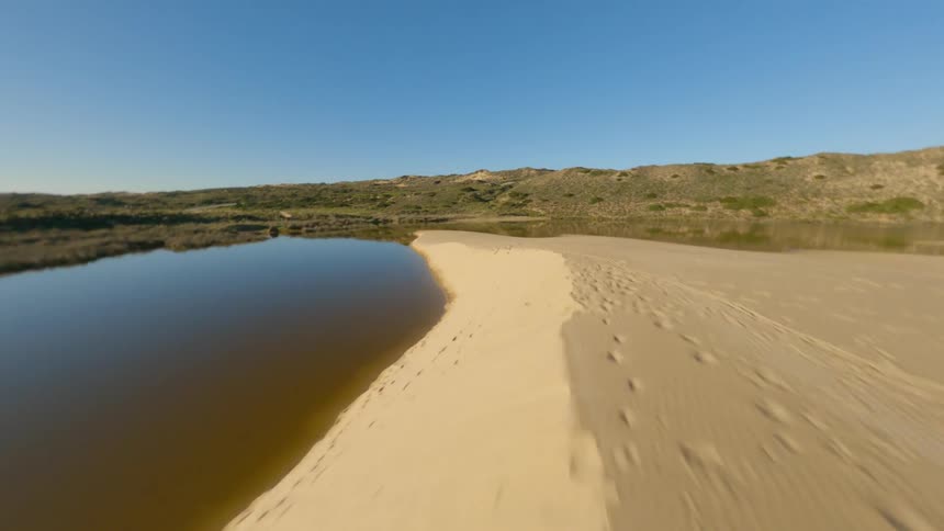 Reflective water surrounds sand while bordered by hills