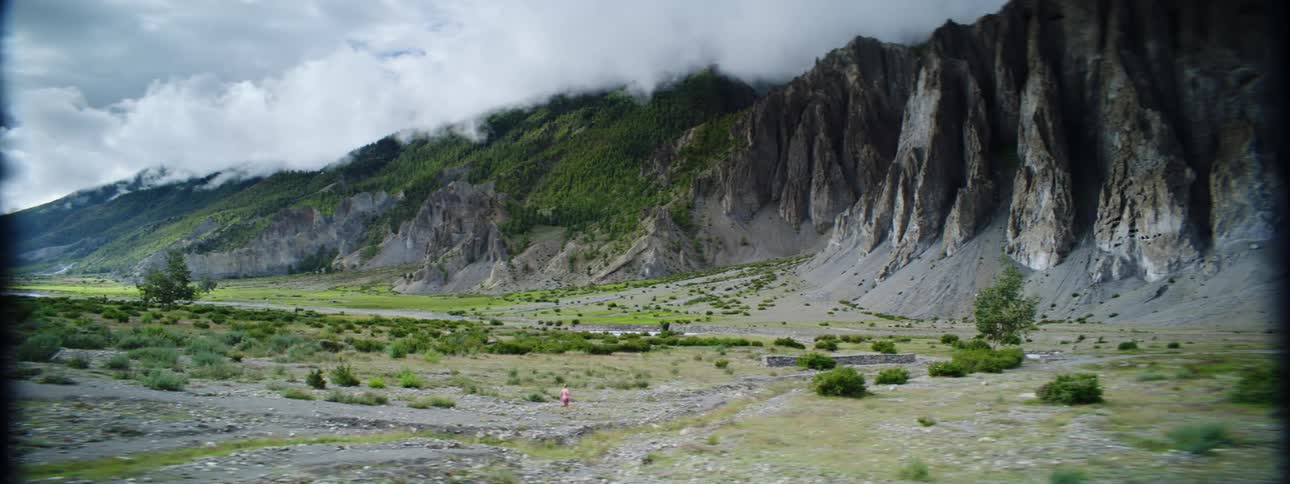 A girl runs through a mountain valley toward a cliff on a cloudy day