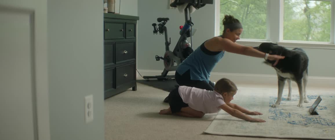 Dog watches mother and daughter exercise on bedroom rug while watching tablet
