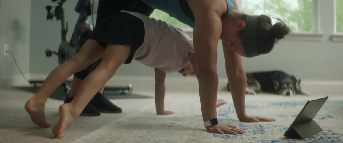A little girl crawls under her mother who is exercising at home