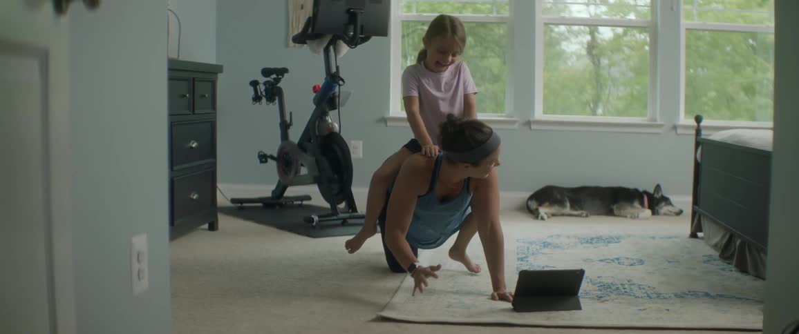 A young girl rides on her mothers back as the woman sits on all fours and stretches her arms out