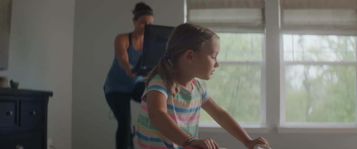 Mother and daughter exercise on stationary bikes in room with windows