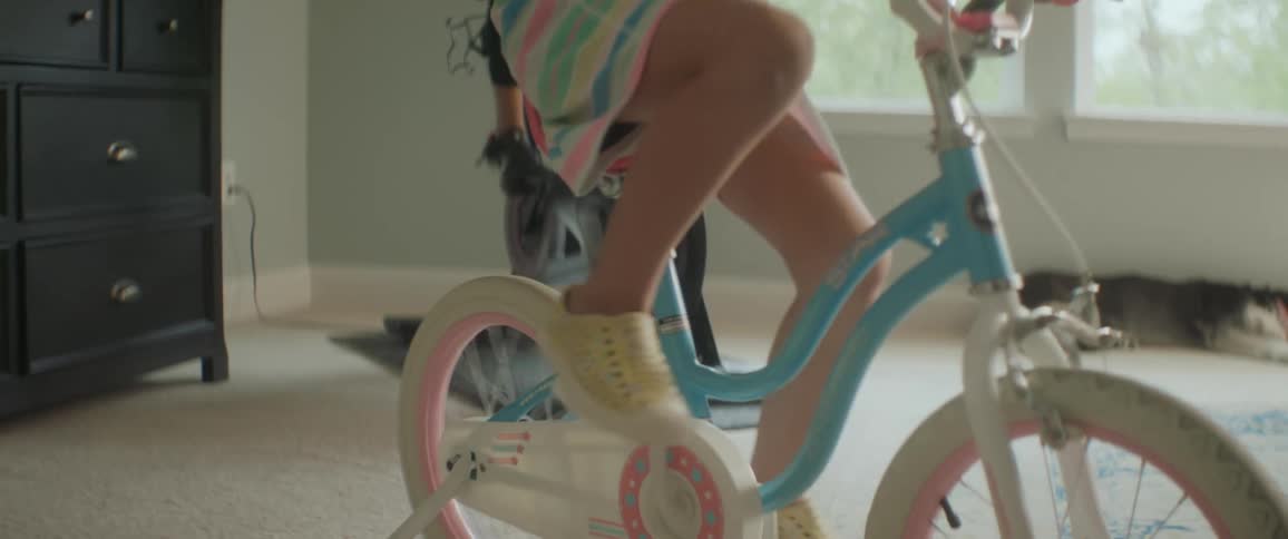 A young girl laughs and smiles as she rides her bicycle turned into a stationary bike alongside her mom