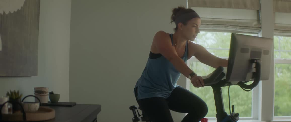 A young woman works out on a smart exercise bike in a home living room during the day