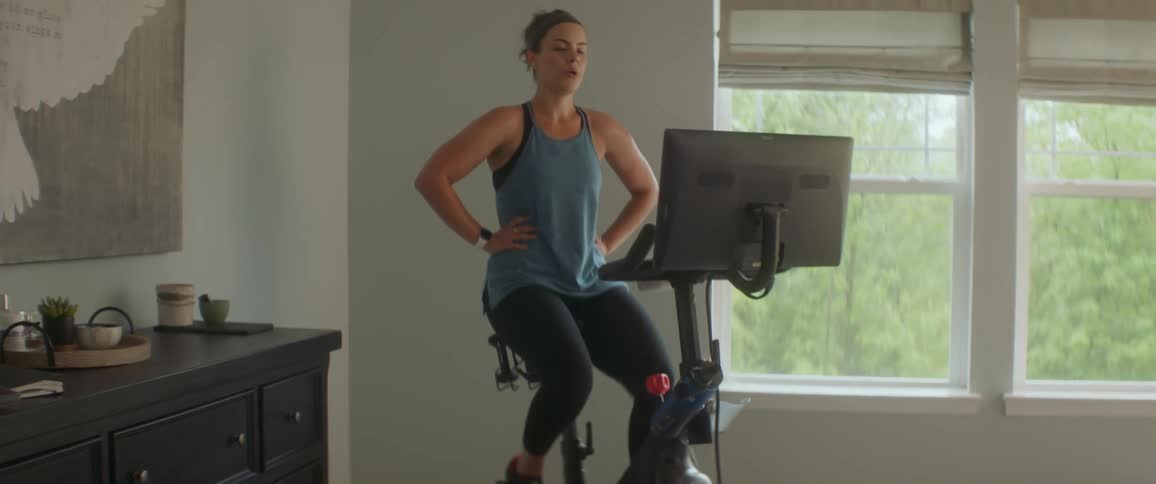 Woman exercises on exercise bike near windows adjusting machine settings