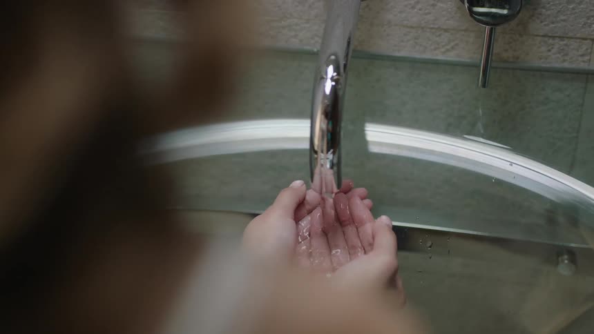 Water running into cupped hands in a bathroom sink