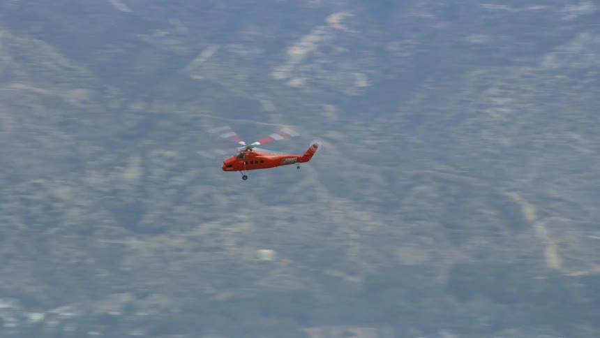 A Sikorsky S58T helicopter flies over mountains in Pacoima California in aerial footage