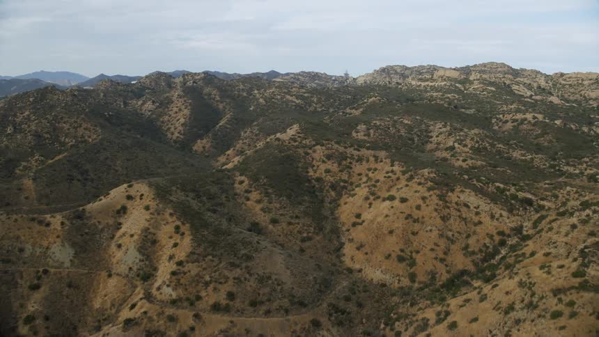 Aerial footage of Canoga Park California during summer showcasing brown hills and trees with heavy clouds over the mountains
