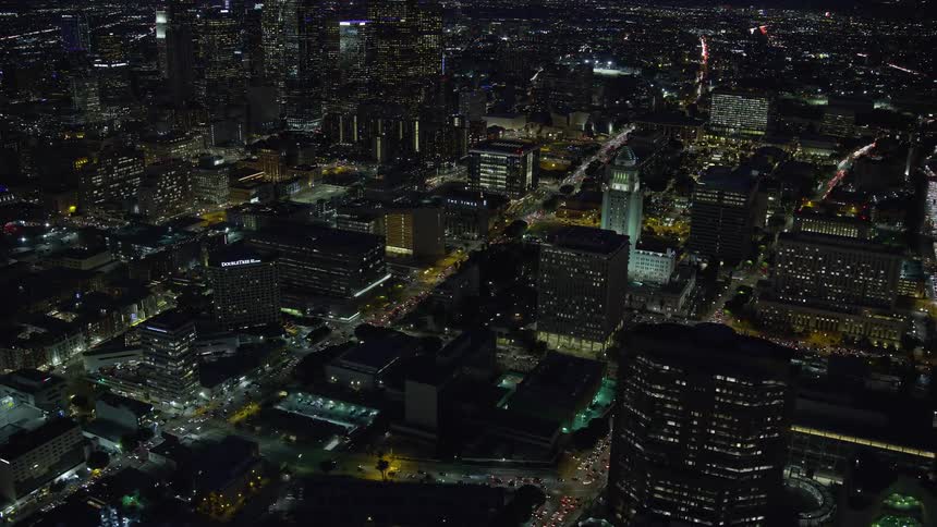 A stunning aerial shot of Downtown LA at night flying by City Hall and approaching LAPD headquarters with skyscrapers and city lights visible in the background