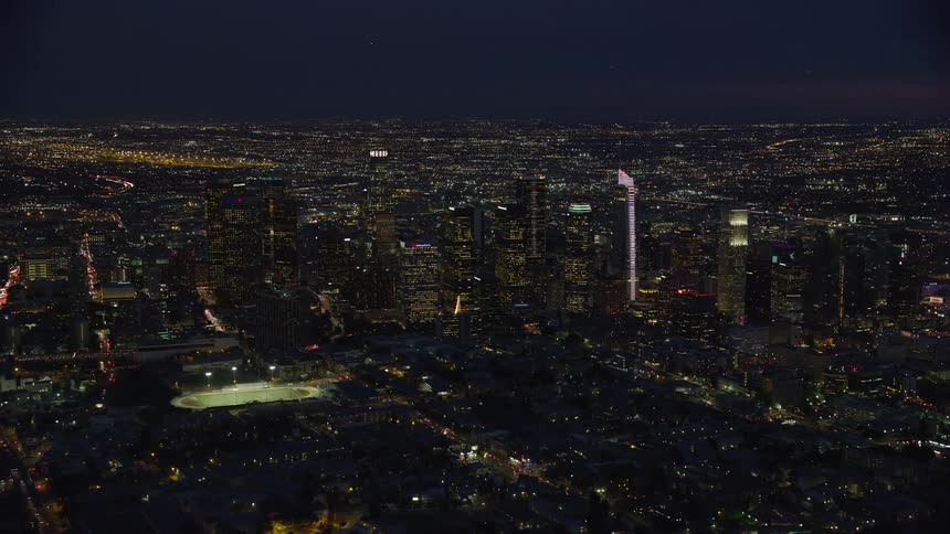 Aerial footage of illuminated skyscrapers in downtown Los Angeles California captured during a partly cloudy night
