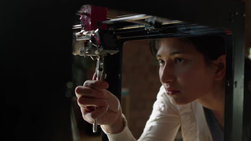 A woman uses a wrench to tighten a screw under a table