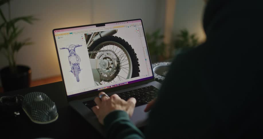 A man is sitting at a desk working on a laptop computer with an image of a motorcycle