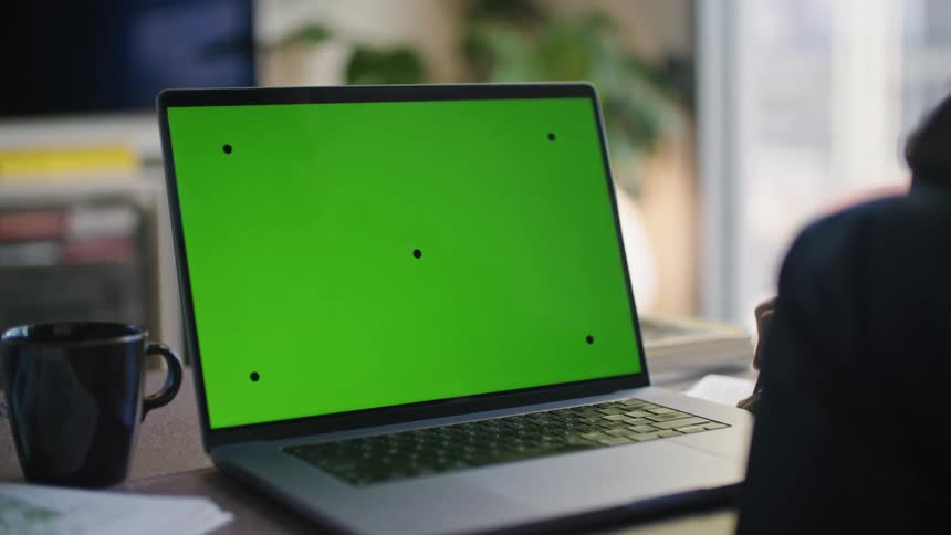 Woman writes while sitting at desk in front of a laptop