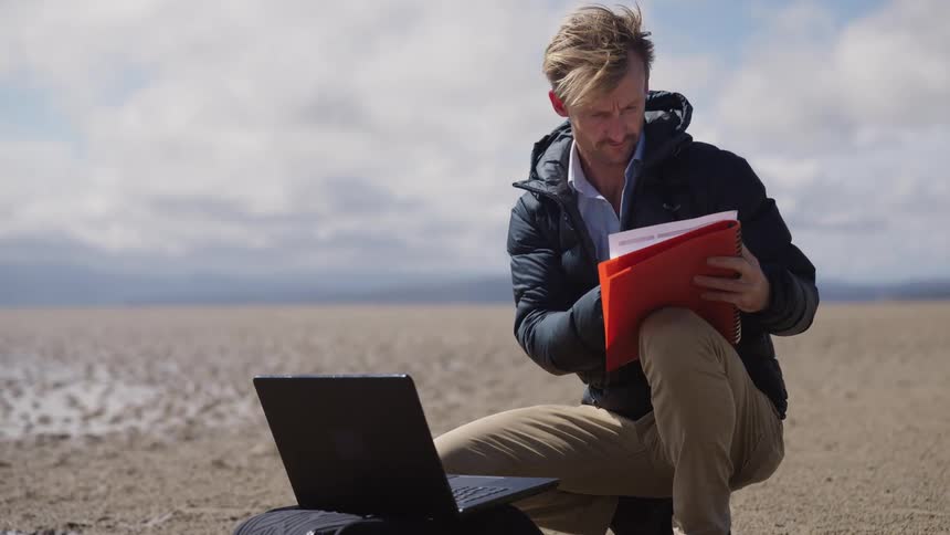 A man is using a laptop and taking notes outside