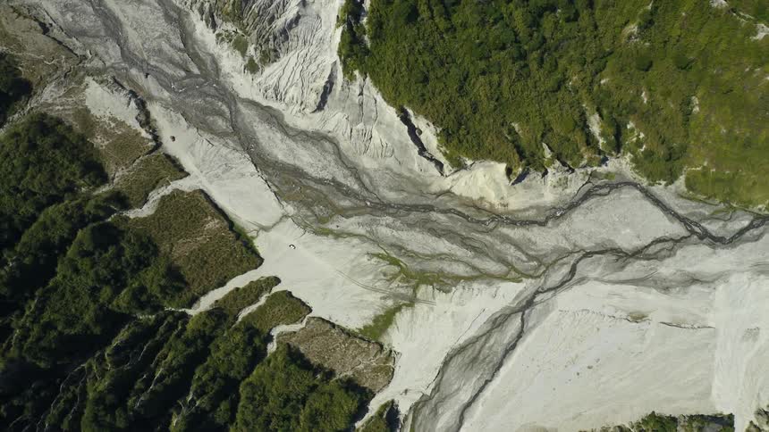 Scenic view of glacier snow and river winds through forested mountains and past sheer rocky cliffs