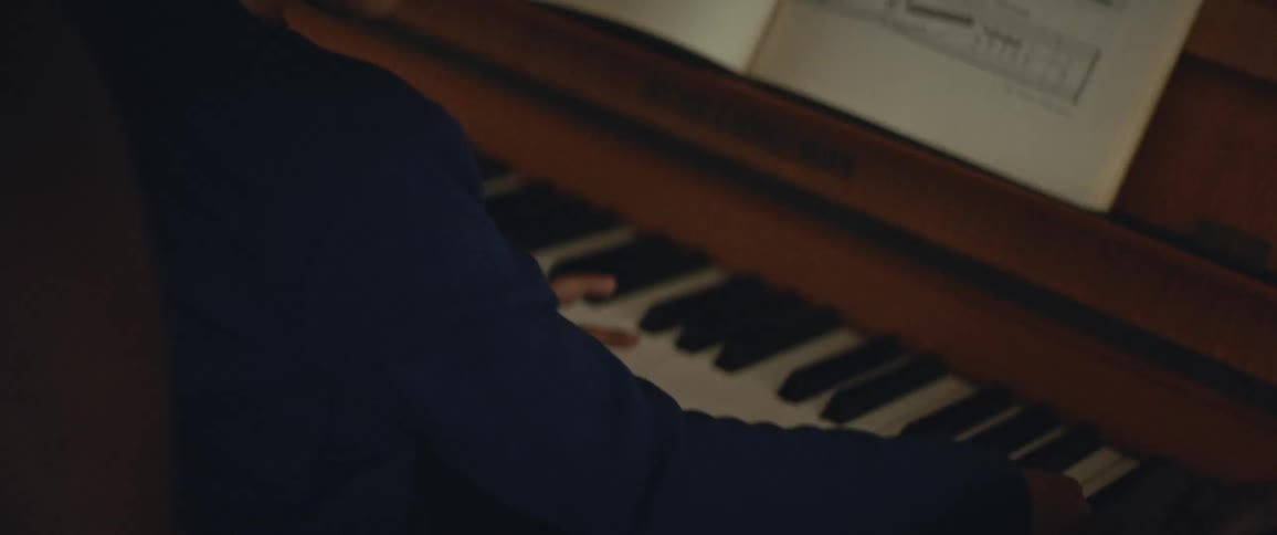 A father teaches his young son how to play the piano while the son sits on fathers lap