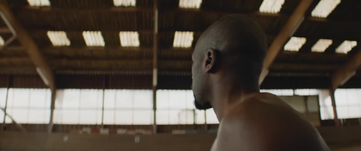 A man moving around a large empty hall while shirtless
