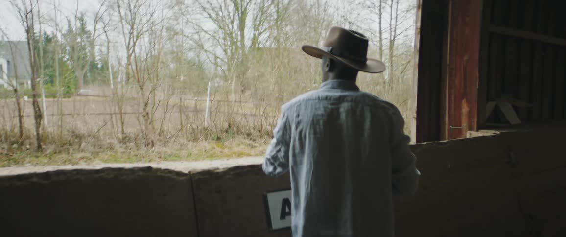 A man is wearing a hat and looking outside from his window as if lost in thought or enjoying the view