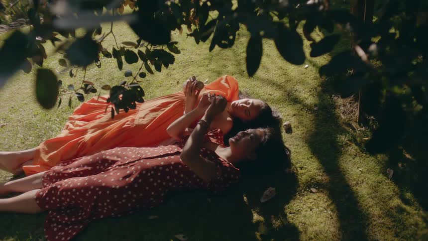 Two women lie on their backs under tree examining shells