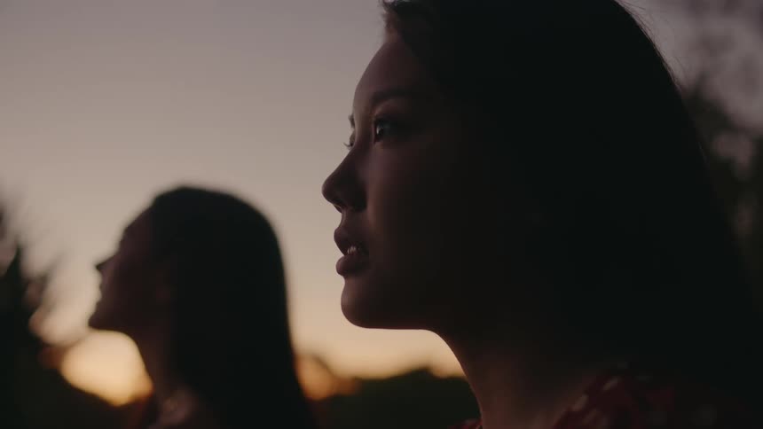 Two girls stand outside at dusk and stare intensely at something off camera while smiling