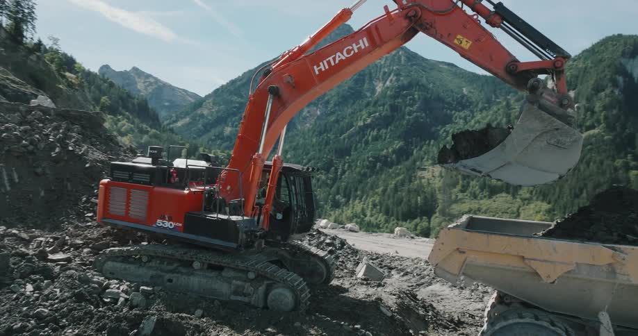Red excavator crane digging out the side of a volcanic rock formation during midday in the mountains