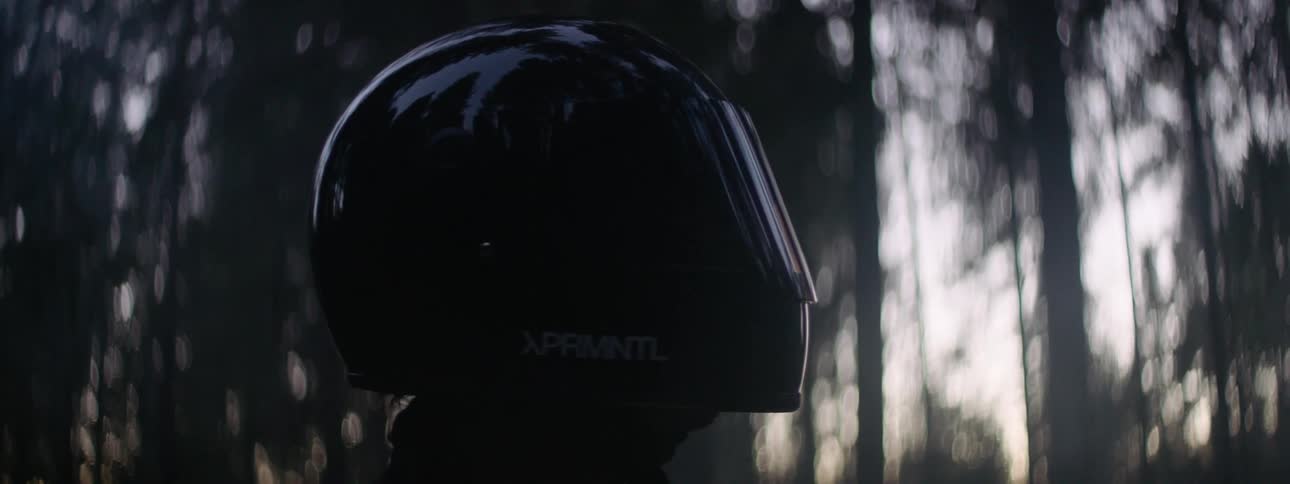 Person wearing a crash helmet with the visor down looks around woods