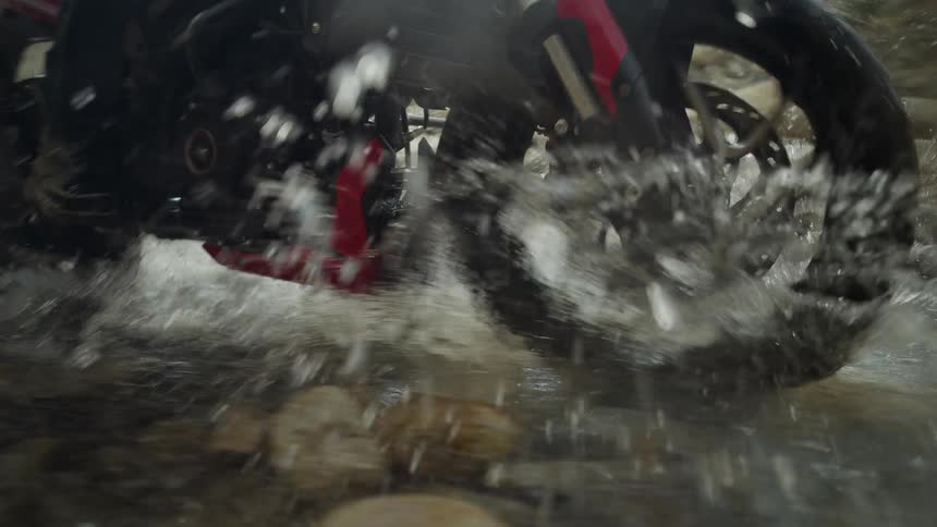 A person is riding their motorcycle through a puddle
