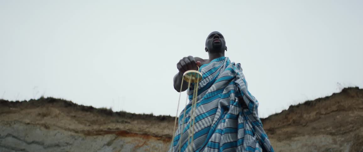 Man wearing a white and blue robe swings an incense burner in front of a cliff