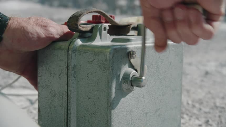 A man holds a small hand cranked power generator as he quickly rotates its handle