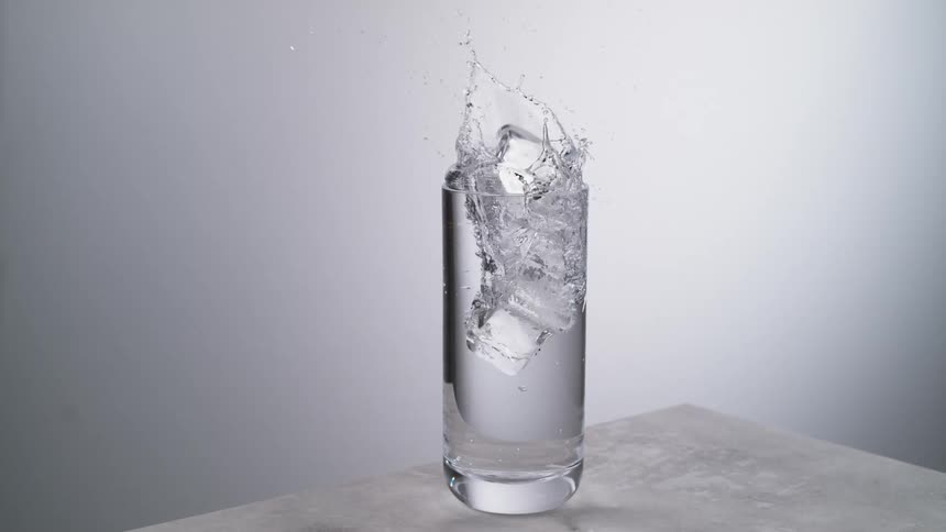 The ice cubes fall into the glass of water
