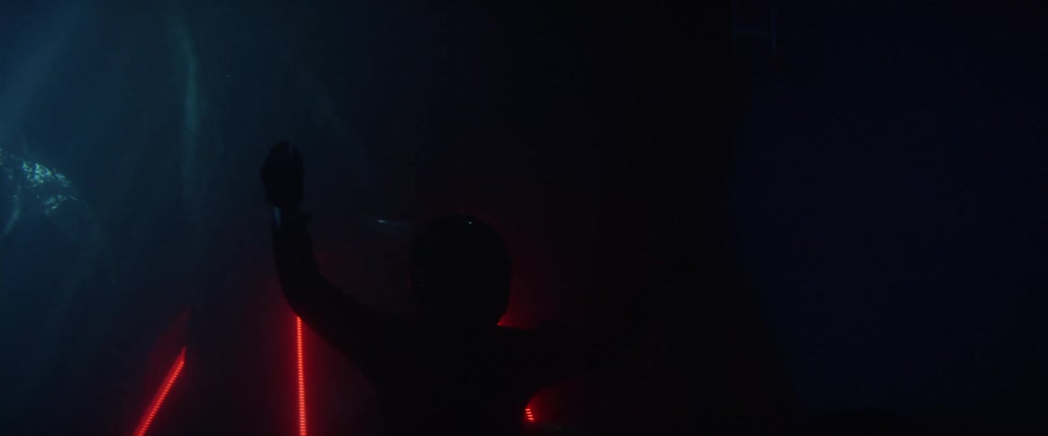 Person wearing a crash helmet floating in dark water swims toward surface as light shines downward
