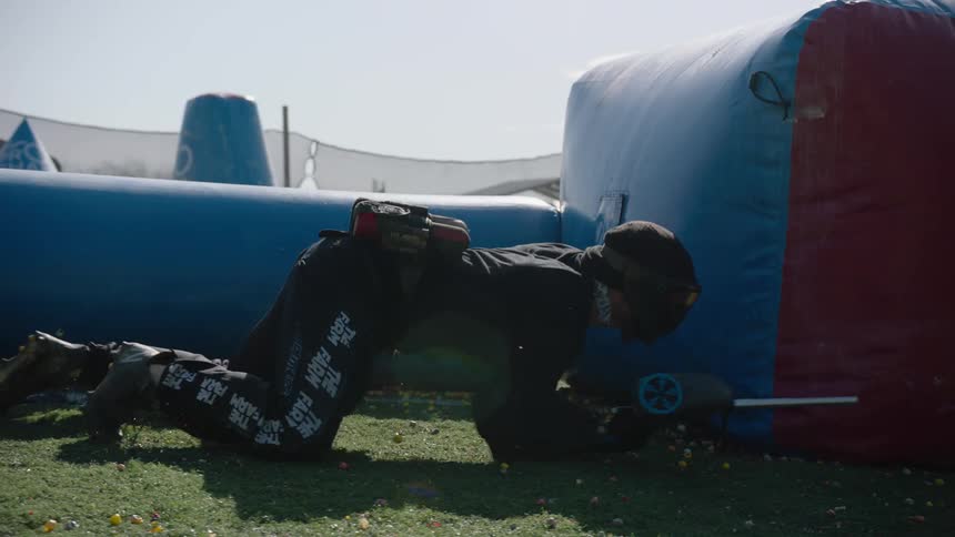 A teenager wearing a helmet with goggles and a paintball gun moves behind barriers in the gaming zone as he sneaks around ready to shoot