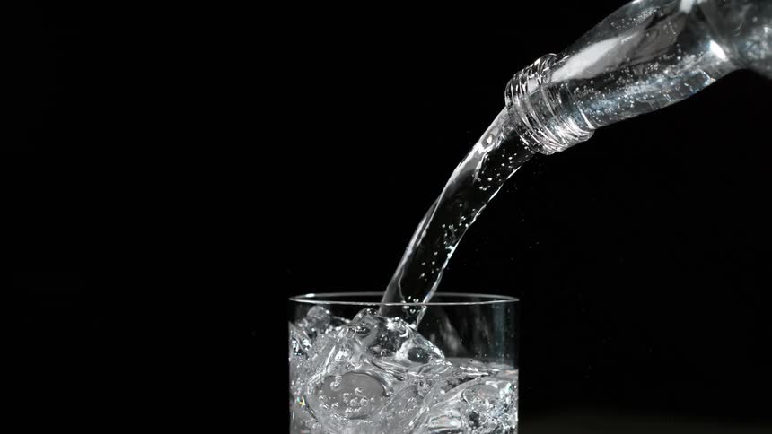Water pours from a clear water bottle into a chilled glass cup filled with ice cubes creating a refreshing and thirstquenching beverage perfect for any hot day
