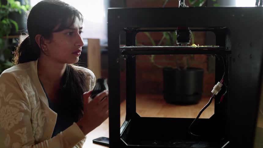 Young long haired woman inspects very closely a 3d printer in the office
