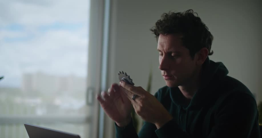 A man picks up a gear to examine while working on his laptop